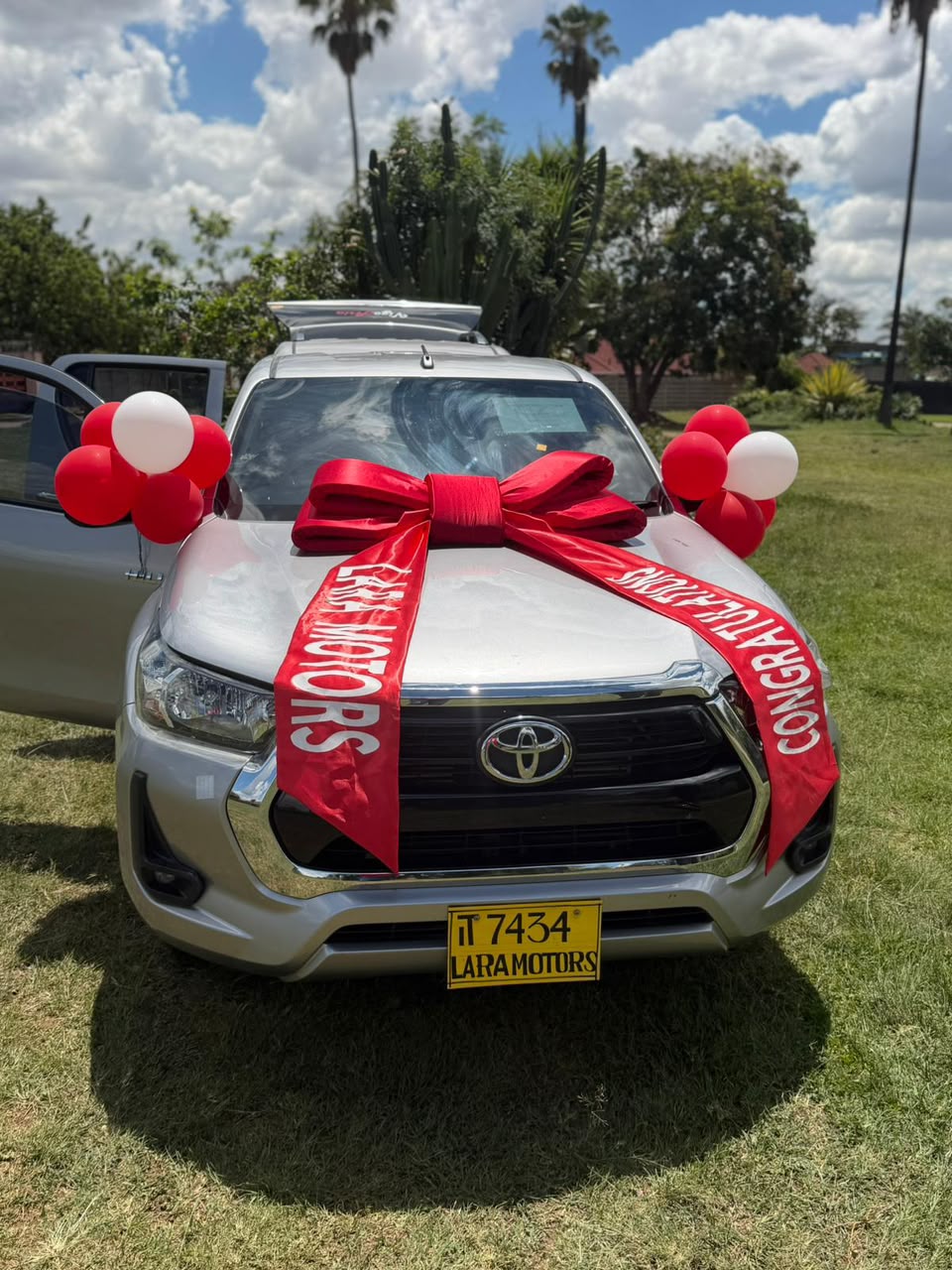 Silver Toyota Hilux with red Lara Motors congratulations ribbon and balloons