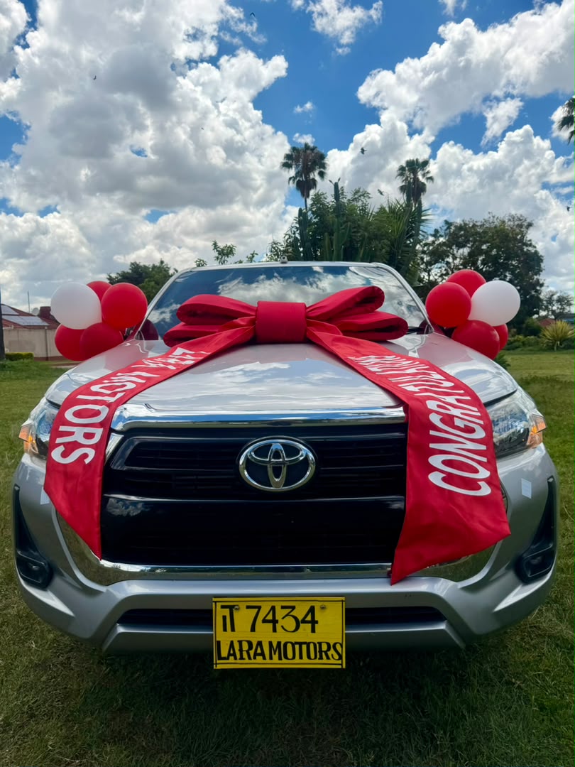 Silver Toyota Hilux with red bow and balloons under a blue sky