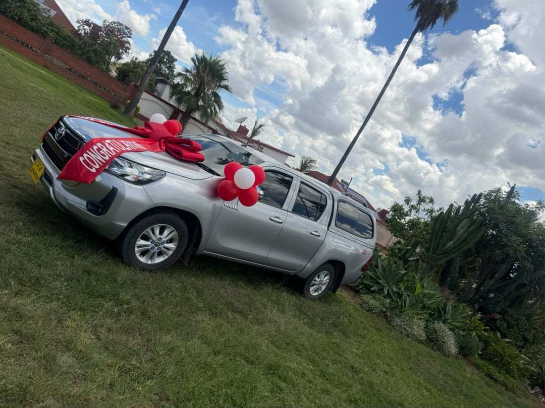 Silver Toyota Hilux with red congratulations ribbon and balloons on a lawn