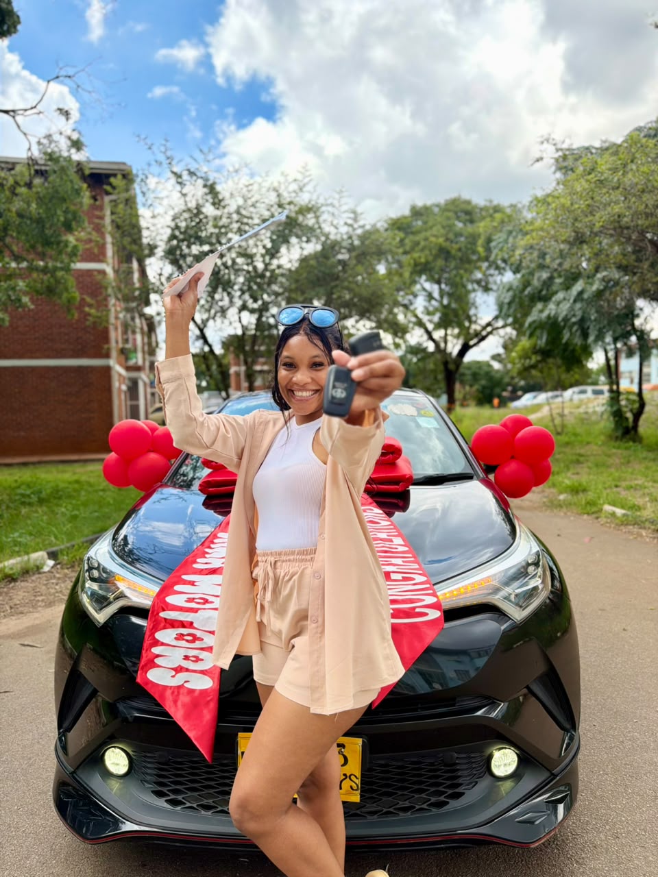 Excited customer holding keys in front of a black Toyota C-HR with red Lara Motors ribbon