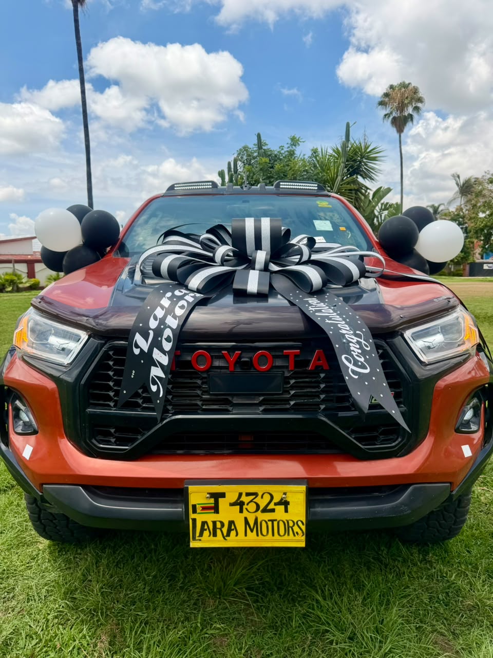 Red Toyota Hilux with black and white Lara Motors congratulations ribbon