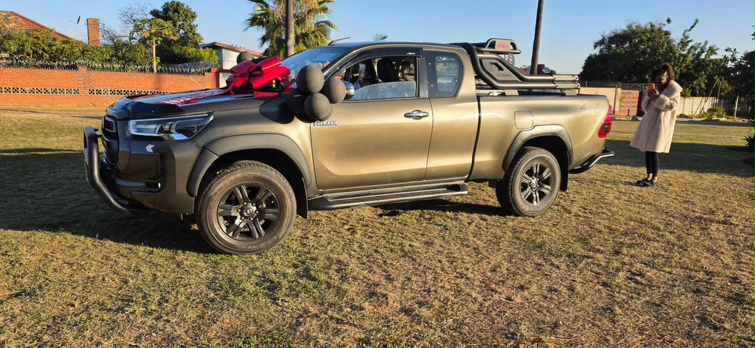 Bronze Toyota Hilux extra cab with red Lara Motors ribbon on a lawn